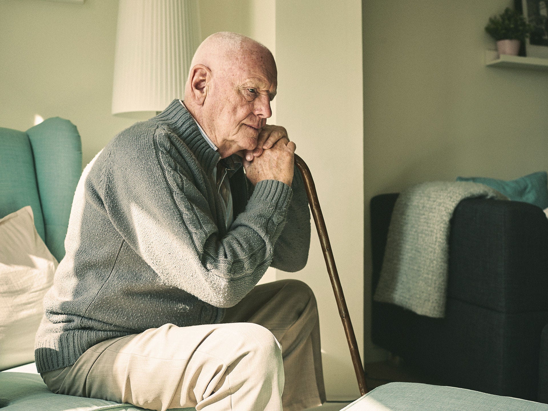 Ein älterer Mann sitzt erschöpft in einem Sessel und stützt sich auf seinen Gehstock. Ab einem Alter von 60 Jahren steigt das Risiko für einen schweren Corona-Krankheitsverlauf.