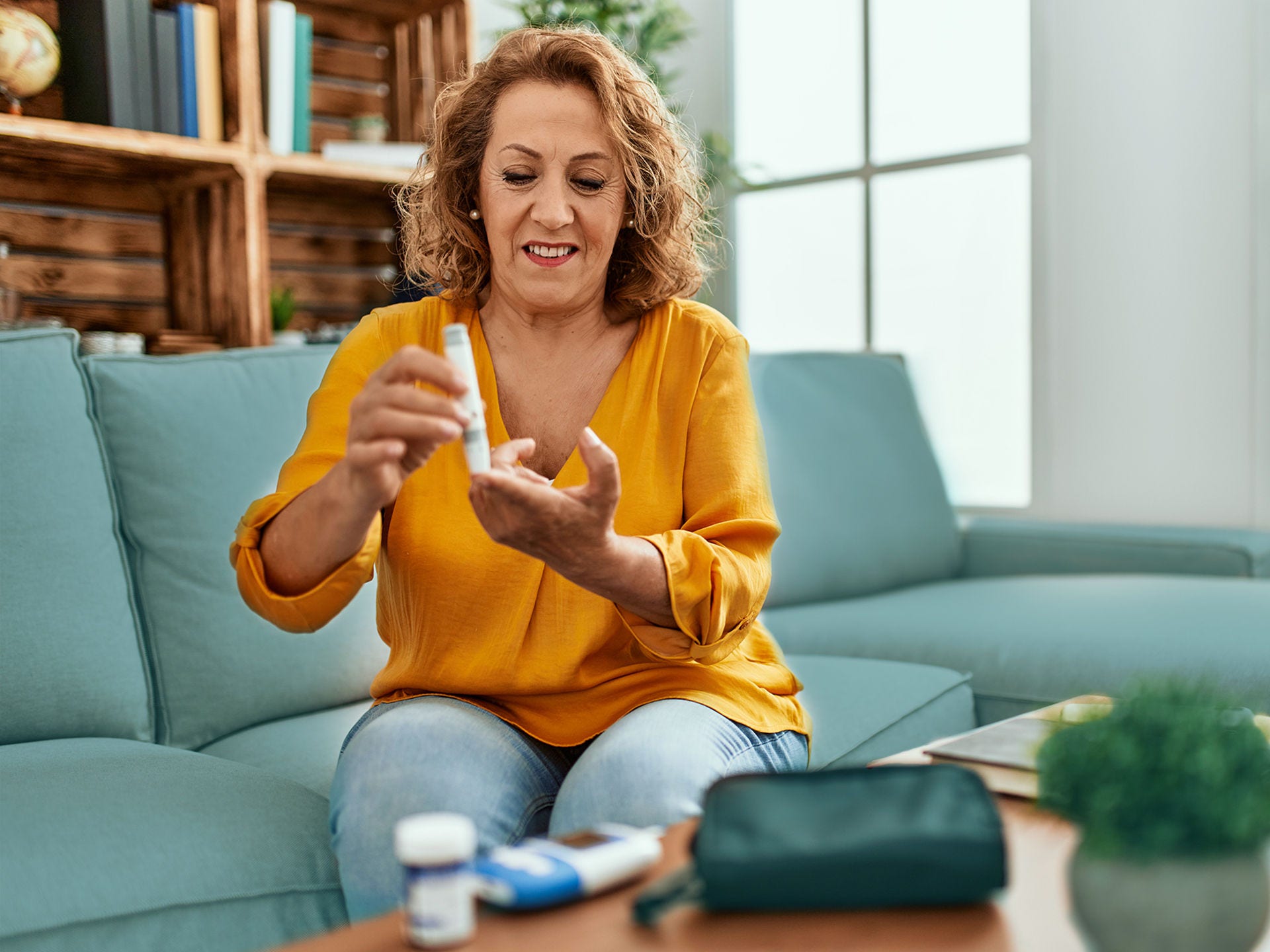 Ein ältere Frau sitzt zuhause auf ihrem Sofa und misst ihren Blutzucker. Menschen mit Diabetes haben ein erhöhtes Risiko für einen schweren Corona-Krankheitsverlauf.