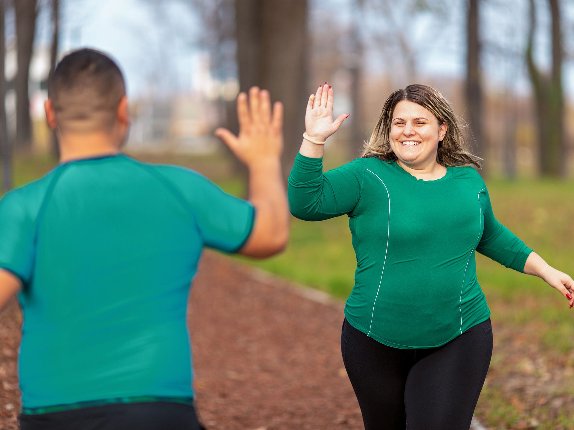 Frau mit Adipositas joggt im Freien und gibt einer anderen joggenden Person ein High Five. Gewichtsreduktion kann dazu beitragen, das Risiko für einen schweren Corona-Krankheitsverlauf zu verringern.